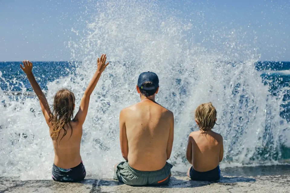 A couple of kids sitting on top of a beach next to the ocean