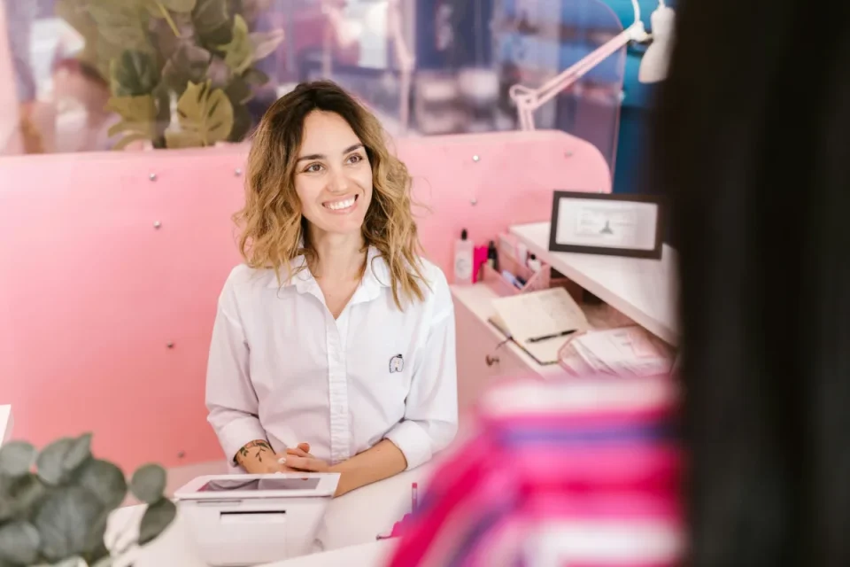 Smiling beauty salon receptionist sitting behind a pink front desk and talking to a client