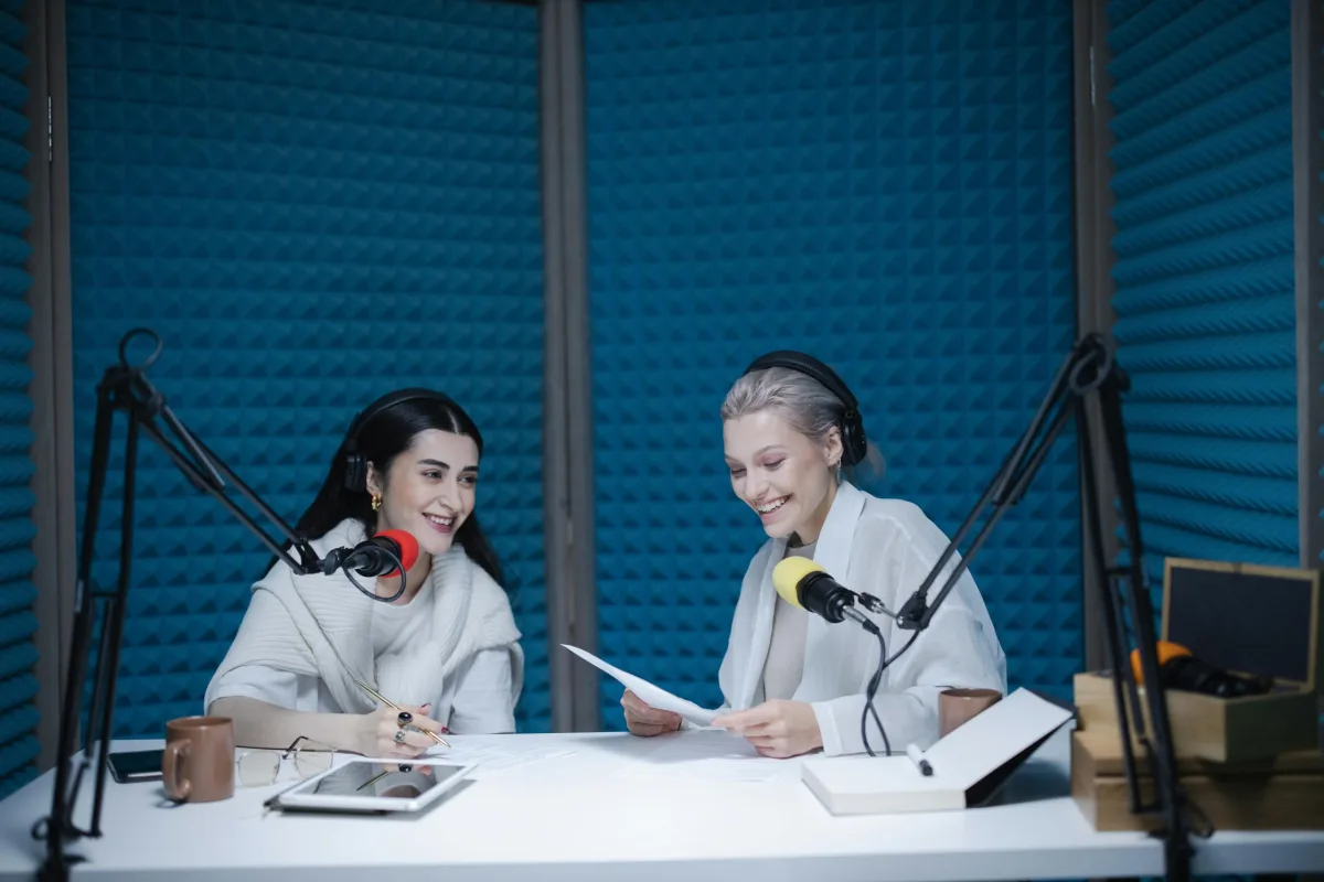 Two women recording a podcast in a soundproof studio, speaking into professional microphones.