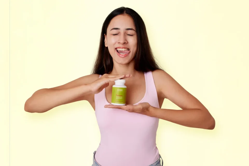 Smiling woman holding a green dietary supplement bottle in her hands against a light background