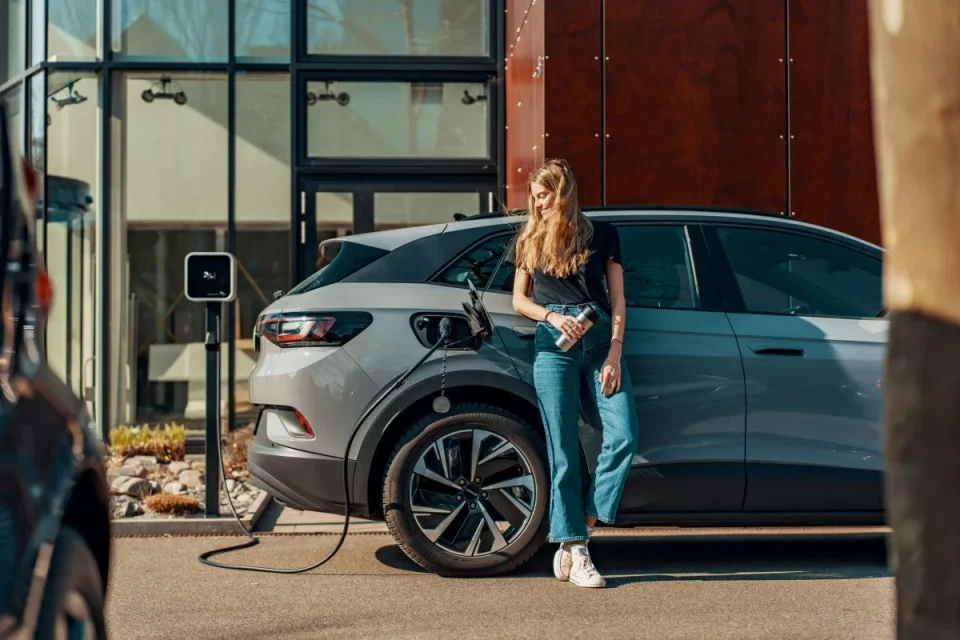 Woman charging an electric car at a home charging station in front of a modern house