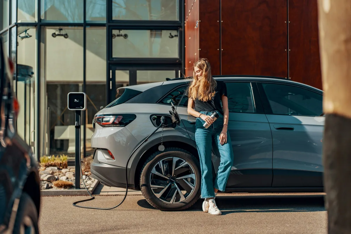 Woman charging an electric car at a home charging station in front of a modern house