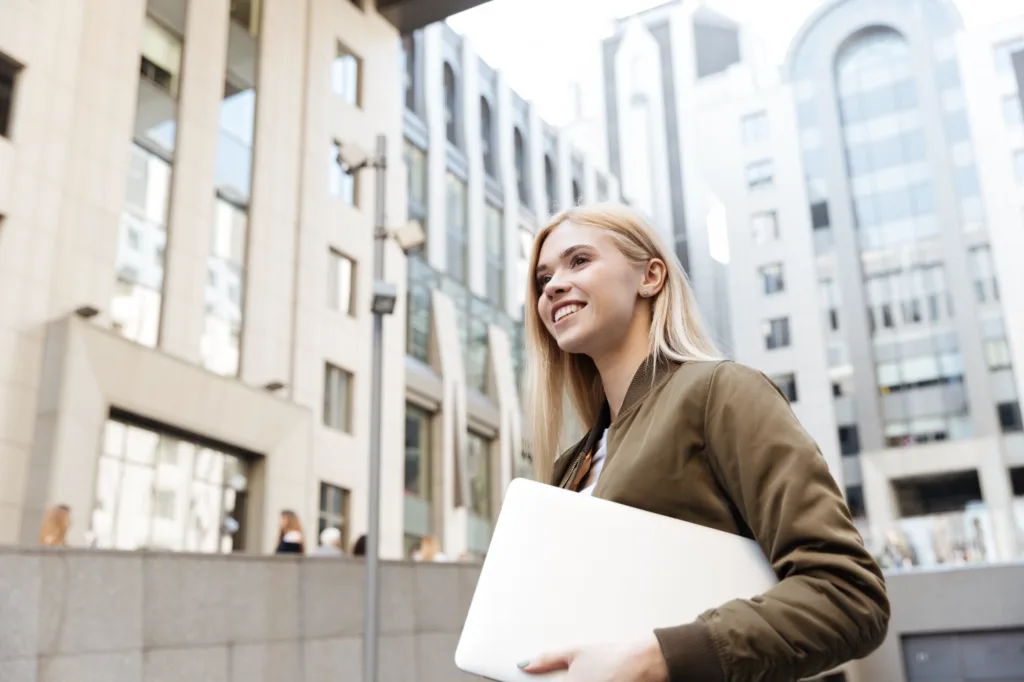 Woman holding a laptop in an urban setting, representing modern business communication and international mobility
