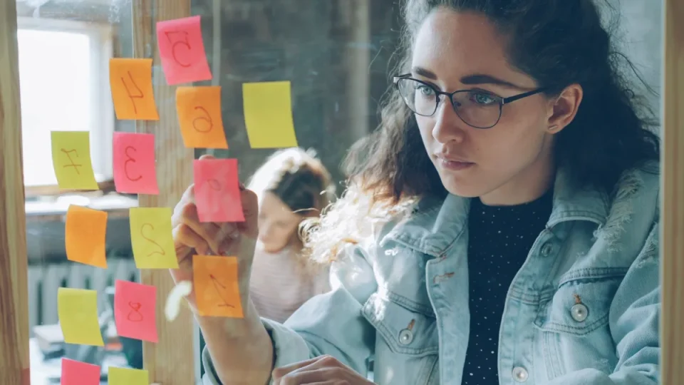 Woman organizing a project using colorful sticky notes on a glass wall