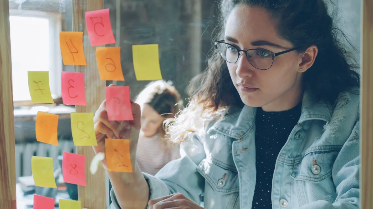 Woman organizing a project using colorful sticky notes on a glass wall