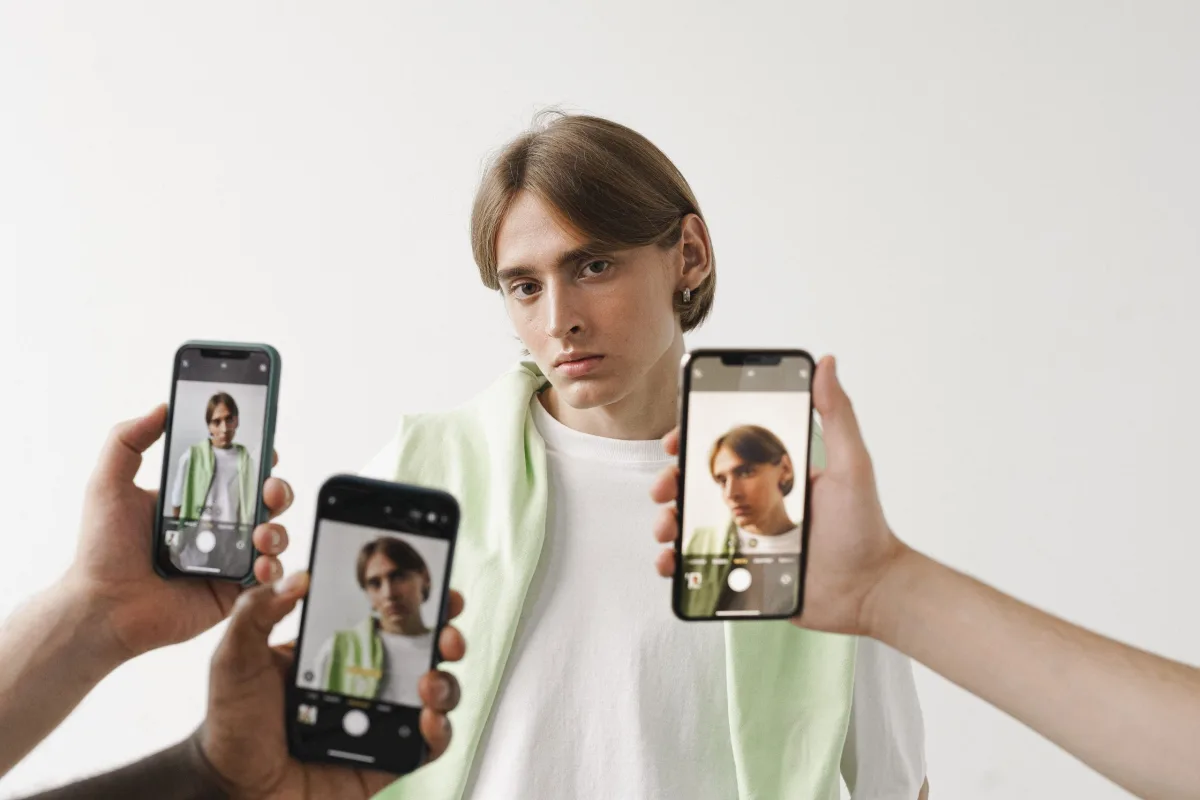 Person posing while being photographed with multiple smartphones